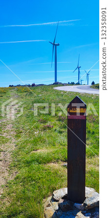 Hiking trail marker on a hill in northern Portugal. Wildflowers with wind turbines - ecotourism, renewable energy and nature adventure trail in Portugal Hiking trail marker on a hill in northern Portugal. Wildflowers with wind turbines - ecotourism, renewable energy and nature adventure trail in Portugal 132358091