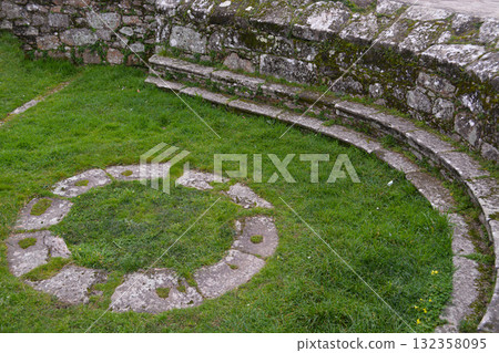 An old stone path in a circular pattern on green grass in a park in Spain. Concept for decorative landscaping and tourism. 132358095