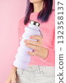 Woman holding collapsible reusable lilac water bottle on pink background. Sustainable lifestyle 132358137