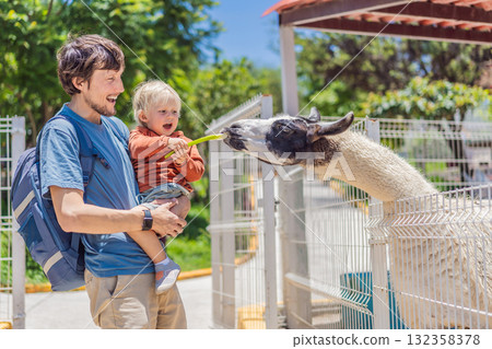 Father and son feeding a llama on a farm, enjoying family bonding, animal interaction, and outdoor activity. Wholesome childhood and learning concept Father and son feeding a llama on a farm, enjoying family bonding, animal interaction, and outdoor activity. Wholesome childhood and learning concept 132358378
