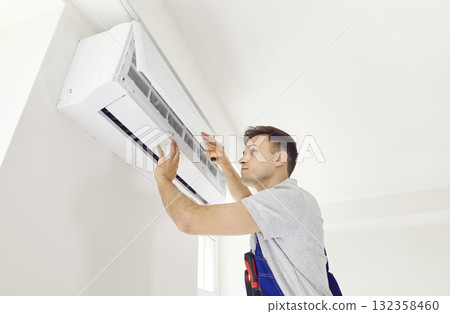 Portrait of smiling electrician with screwdriver maintaining air conditioner indoors. 132358460