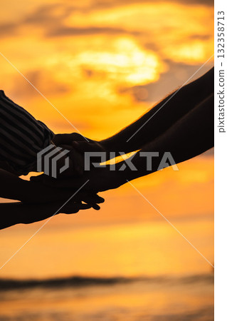 Close-up of hands stacked together in a gesture of unity and support against a glowing sunrise over the sea. Close-up of hands stacked together in a gesture of unity and support against a glowing sunrise over the sea. 132358713