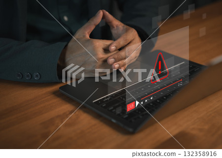 User using a laptop computer with a glowing warning error icon and live stream interface, symbolizing cyber security alert, system error, online risk, technology problem and digital safety. User using a laptop computer with a glowing warning error icon and live stream interface, symbolizing cyber security alert, system error, online risk, technology problem and digital safety. 132358916