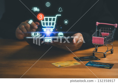 Customer using tablet with shopping cart icon, credit cards, and miniature trolley symbolizing online shopping, e-commerce, payment, retail, digital marketplace, delivery and modern technology. 132358917