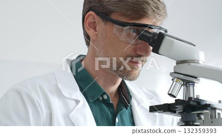 Senior man scientist wearing protective glasses and lab coat analyzing samples with a microscope in laboratory setting. Medicine, health care and science concept 132359393