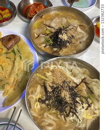 Warm bowl of Mandu-guk, a traditional Korean soup with soft dumplings, sliced rice cakes, and green onions in a savory broth. Comforting and flavorful, perfect for a hearty meal. 132362733