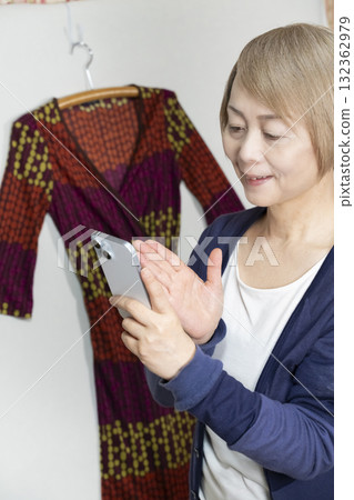 一位老年婦女用智慧型手機拍攝不想要的衣服，準備在跳蚤市場上販售 132362979