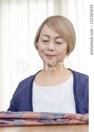 A senior woman packing unwanted clothes in the living room to sell them on a flea market site A senior woman packing unwanted clothes in the living room to sell them on a flea market site 132363055