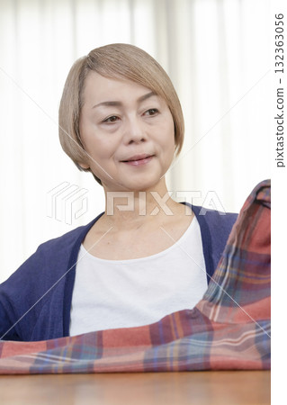 一位老年婦女在客廳打包不想要的衣服，準備在跳蚤市場上販售 132363056