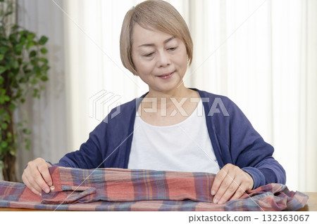 一位老年婦女在客廳打包不想要的衣服,準備在跳蚤市場上販售 一位老年婦女在客廳打包不想要的衣服,準備在跳蚤市場上販售 132363067