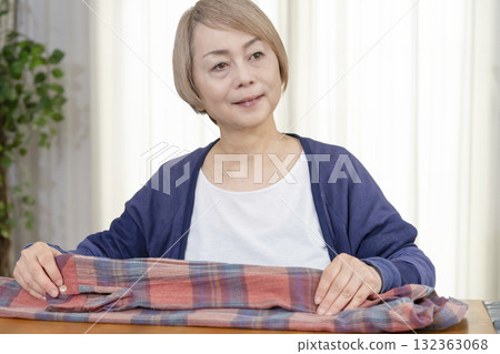 一位老年婦女在客廳打包不想要的衣服,準備在跳蚤市場上販售 一位老年婦女在客廳打包不想要的衣服,準備在跳蚤市場上販售 132363068