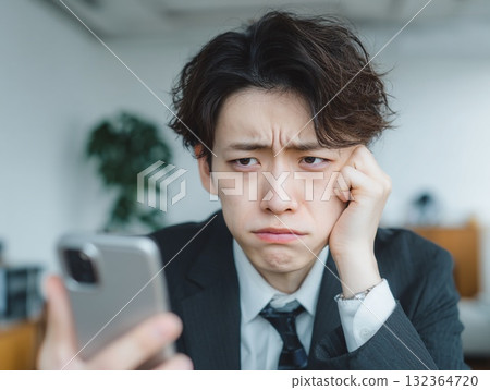 A businessman with a troubled expression looks worried while looking at his smartphone 132364720