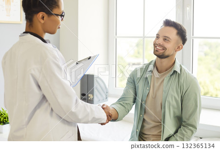 Friendly doctor shaking hands with a young patient standing in medical clinic 132365134