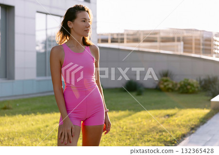 Portrait of attractive woman in pink outfit enjoying outdoor activity at sunset in the park. 132365428