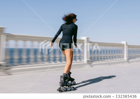 Woman rollerblading along seaside promenade in black outfit, active lifestyle and freedom concept Woman rollerblading along seaside promenade in black outfit, active lifestyle and freedom concept 132365436