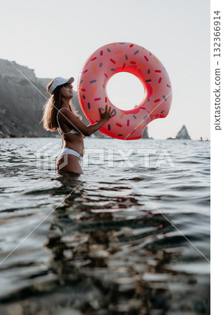 Woman, water, donut float, happy woman holding a donut float in the sea with rocky cliffs, enjoying summer vacation 132366914