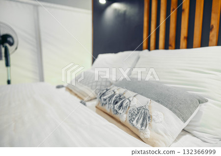 Cozy glamping tent interior with a neatly made bed. Soft pillows and a wooden headboard create a comfortable atmosphere for relaxation. 132366999