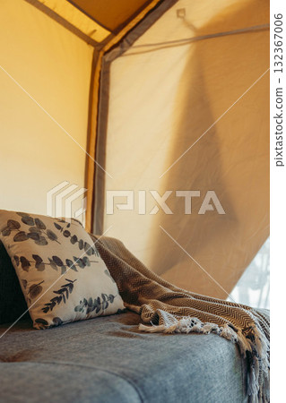 Cozy glamping tent interior with a comfortable sofa, decorative pillow, and a warm blanket. Soft lighting creates a relaxing atmosphere. Cozy glamping tent interior with a comfortable sofa, decorative pillow, and a warm blanket. Soft lighting creates a relaxing atmosphere. 132367006