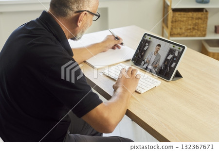 Mature man on video call during online meeting, tablet on desk for coaching Mature man on video call during online meeting, tablet on desk for coaching 132367671