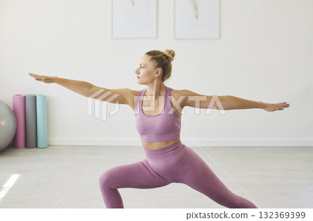 Young woman practicing yoga warrior pose in a bright home fitness studio 132369399