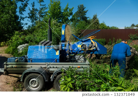 An operator loads tree branches into a wood chipper. An operator loads tree branches into a wood chipper. 132371849