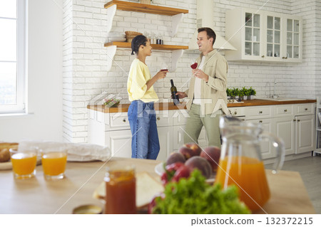 Happy couple toasting wine together in bright home kitchen, enjoying family time Happy couple toasting wine together in bright home kitchen, enjoying family time 132372215
