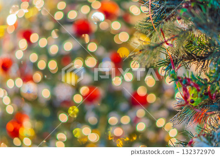 A blurry, out-of-focus photograph of a decorated Christmas or New Year's tree, adorned with ornaments and garlands that glow and sparkle, creating a bokeh effect. Background shot, out of focus. A blurry, out-of-focus photograph of a decorated Christmas or New Year's tree, adorned with ornaments and garlands that glow and sparkle, creating a bokeh effect. Background shot, out of focus. 132372970