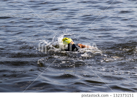 Person Swimming in Open Water With Splashes and a Bright Yellow Cap 132373151