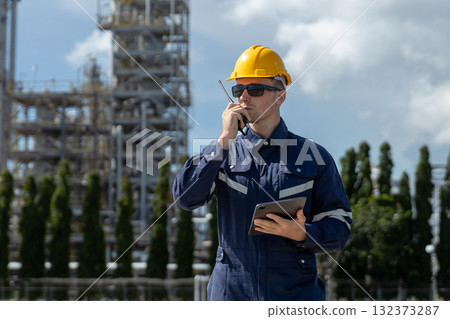 Engineer wearing safety helmet using walkie-talkie and tablet in industrial plant area, representing communication, safety management, inspection process and refinery oil plant factory operation. 132373287