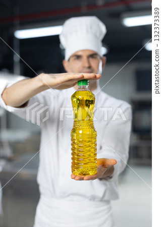 Close up bottle of cooking oil in a hand chef. culinary professional stands in equipped kitchen showing cooking vegetable olive oil. 132373389