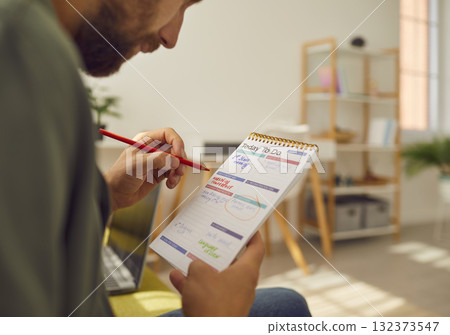 Young businessman sitting on sofa at home or at office planning tasks and to do list in notepad. Young businessman sitting on sofa at home or at office planning tasks and to do list in notepad. 132373547