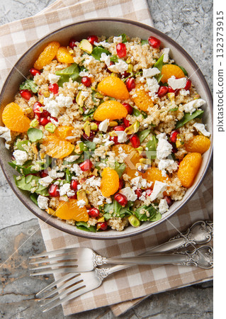 Vegetarian quinoa salad with fresh spinach, feta, tangerines, pomegranate and pistachios close-up in a bowl on the table. Vertical top view 132373915