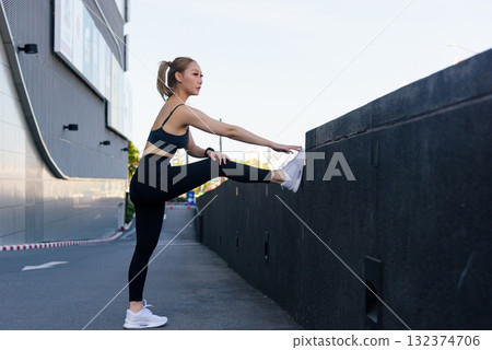 Fit sport woman performs outdoor workout, people stretch for exercise achieving leg flexibility and good body stretch routine with dedication for overall health 132374706