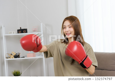 Young happy woman activity at home, people enjoy vibrant exercise training with boxing gloves, developing personal strength and vigorous fitness wellness Young happy woman activity at home, people enjoy vibrant exercise training with boxing gloves, developing personal strength and vigorous fitness wellness 132374797