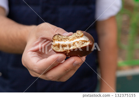 round sponge cake with chocolate in man hand, close up view. Two layers of sponge cake with a marshmallow or souffle layer, covered in chocolate glaze. 132375155