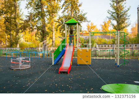 Bright playground features a slide, climbing structure, and spinning feature. Surrounded by colorful autumn trees, this outdoor space is perfect for children's play. improving the quality of life 132375156