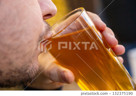 A man drinks dried fruit compote from a glass. Close-up of his mouth. 132375190
