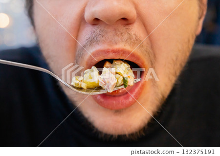 russian Olivier salad on fork and a man with an open mouth close up view. Olivier salad with meat, vegetables and mayonnaise. Traditional russian appetizer for celebrating new year eve and Christmas. 132375191