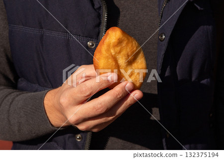 fried potato pie in a man's hands close-up outside 132375194