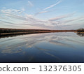 The serene sky and clouds to the horizon are reflected in the quiet river 132376305