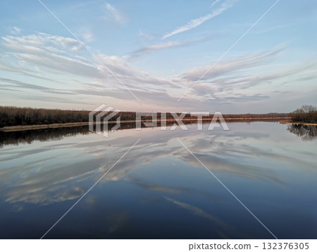 The serene sky and clouds to the horizon are reflected in the quiet river 132376305