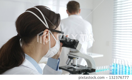Two scientists, a man and a woman, in lab coats and protective gear, conduct research in a sterile laboratory. Concept of medicine and science 132376777