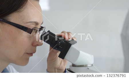 Female researcher focusing on a microscope lens, analyzing scientific samples in a sterile lab for medical innovations. Medicine and science concept Female researcher focusing on a microscope lens, analyzing scientific samples in a sterile lab for medical innovations. Medicine and science concept 132376791