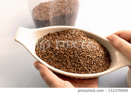 Healthy uncooked raw flax seeds in a bowl in women's hands 132376909