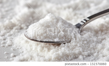 A close-up of a spoon holding a heap of coarse white sea salt crystals, with a powdery texture evident. A close-up of a spoon holding a heap of coarse white sea salt crystals, with a powdery texture evident. 132378860