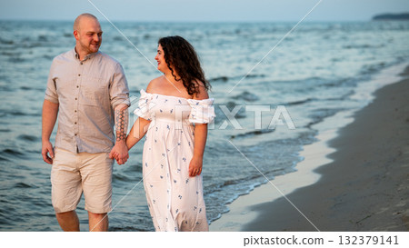 Couple enjoys a romantic evening stroll along the beach at sunset Couple enjoys a romantic evening stroll along the beach at sunset 132379141