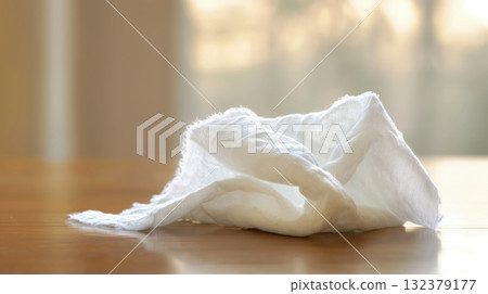 A single crumpled white tissue lies abandoned on a polished wooden table, illuminated by natural light. 132379177