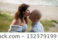 Couple sharing a romantic kiss on a beach during sunset near calm waters and soft grass 132379199