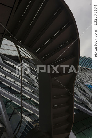 Abstract Structure of Steel Stairs and Glass Building, Artistic steel stairs spiral within a glass structure, casting unique shadows, great for a creative photo or a nature inspired visual promotion. 132379674