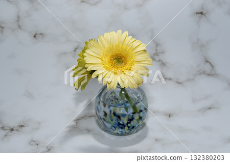 一個冷色調的玻璃花瓶，其後方可見另一朵黃色非洲菊（中心位置）。 132380203